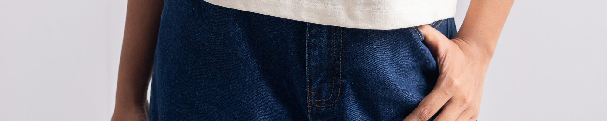 Close-up of a person wearing very wide-leg dark gray denim jeans with diagonal seam details, paired with a white t-shirt. The person is wearing silver rings and a watch.