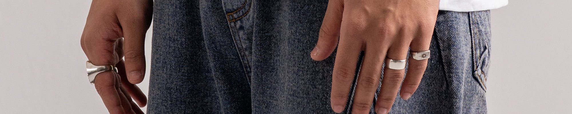 Close-up of a person wearing very wide-leg dark gray denim jeans with diagonal seam details, paired with a white t-shirt. The person is wearing silver rings and a watch.